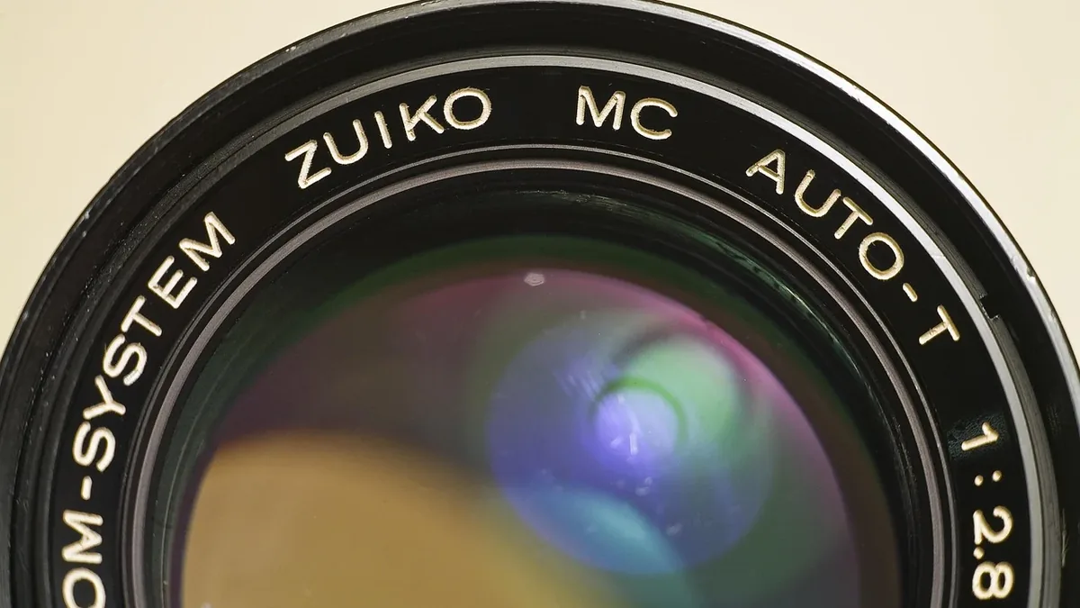 A close-up view of a camera lens with the words "OM-SYSTEM ZUIKO MC AUTO-T 1:2.8" inscribed on it.