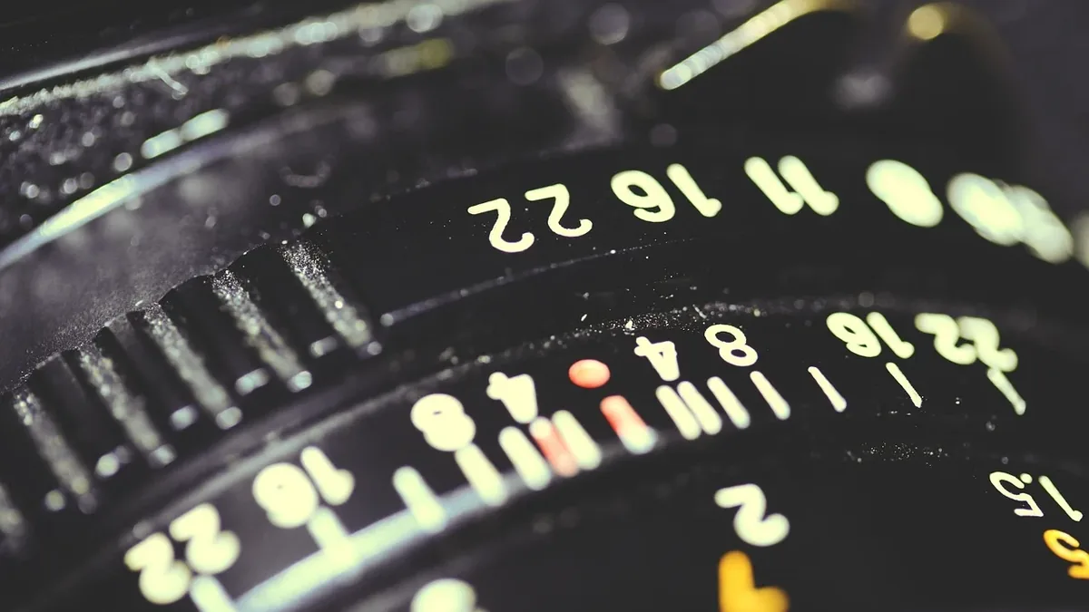 A close-up view of a camera lens's aperture ring, with the numbers 16, 22, 32, 40, 50, 64, 80, and 100 visible.